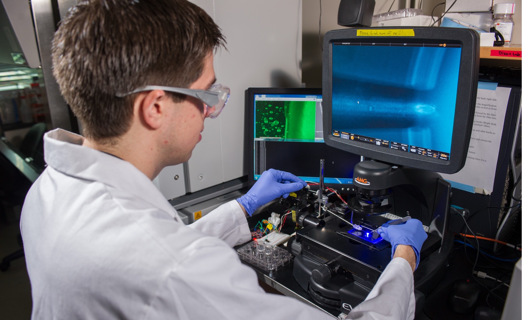 A researcher in a lab setting is wearing protective gear and examine a substance using a machine.